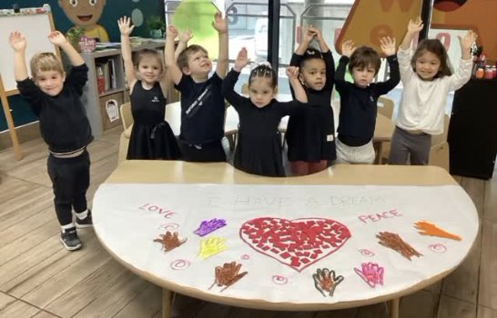 Niños con los brazos arriba junto a su mural con un corazón